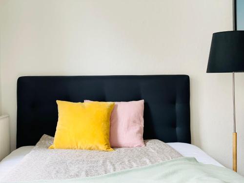 a bed with a black headboard and a yellow and pink pillow at Scandinavian Apartment Hotel -Lunden 2- Central 2 room apartment in Horsens