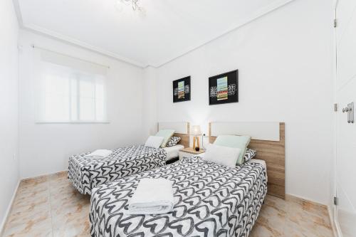 Playa del Pinet Apartment في لا مارينا: سريرين في غرفة بجدران بيضاء