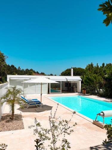 a swimming pool with a white umbrella and a chair and a swimming pool at Edles Apartment in Architektenvilla mit großem Pool, Sauna, Dachterrasse und malerischem Garten in Pataias