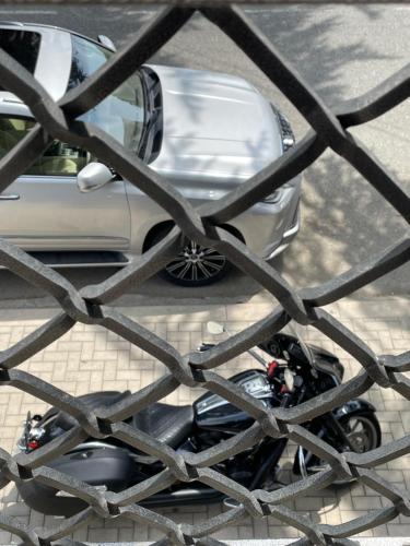 a motorcycle parked next to a car behind a fence at Mini Hotel 7 Street in Sukhum