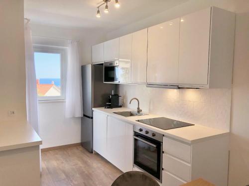 a kitchen with white cabinets and a sink and a window at Apartments Kankul in Krk