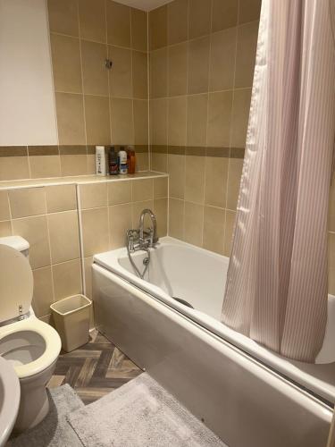 a bathroom with a tub and a toilet with a shower curtain at 2 Bed Apartment Sleeps 5, Free Parking, Free Wifi, Spacious, Quiet, Close to Station, Restaurants & Shops, Contractors and Holidays in London