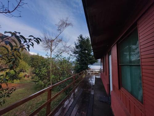 un porche de una casa roja con barandilla de madera en Casita del lago en San Carlos de Bariloche