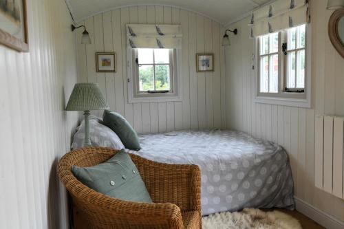 a bedroom with a bed with a wicker chair and two windows at SHEPHERDS HUT in Kent