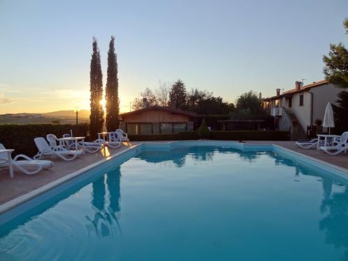 una grande piscina con sedie bianche e un tramonto di Agriturismo Bandinacci a Santa Luce