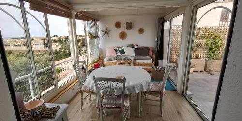 une table et des chaises dans une pièce avec des fenêtres dans l'établissement Maison chaleureuse, vue mer avec belle terrasse,, à Sausset-les-Pins