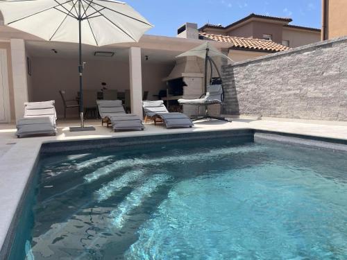 ein Schwimmbecken mit Stühlen und einem Sonnenschirm in der Unterkunft Villa Maslina in Vodnjan