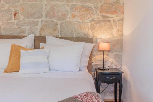 a bed with white pillows and a table with a lamp at Traditional holiday house by the sea in Preko