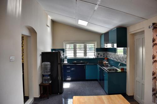 a kitchen with blue cabinets and a black refrigerator at Rochas Valley Homestay in Suntikoppa