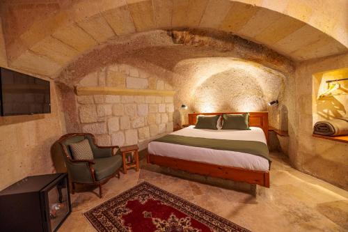 a bedroom with a bed and a chair in a stone room at Canyon Cave Hotel in Urgup