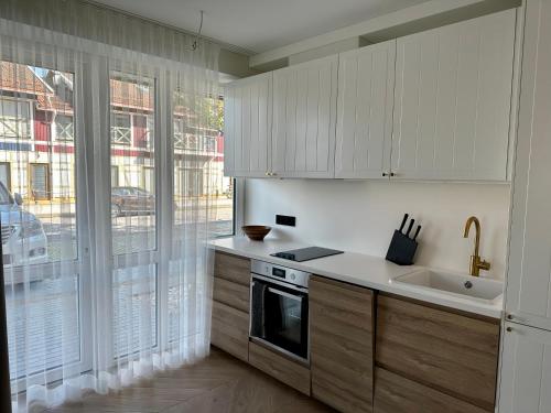 a kitchen with white cabinets and a large window at Nida, Vėtrungių 7 apartamentai prie marių in Nida