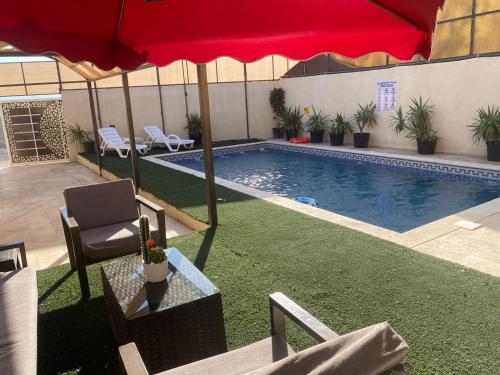 a swimming pool with a red umbrella and chairs at lacasa chalet private With a panoramic view of the DeadSea in Sowayma