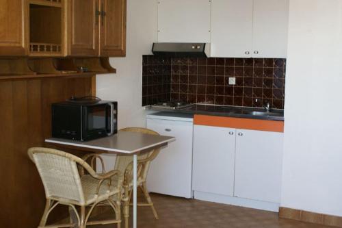 une cuisine avec des armoires blanches et une table avec des chaises dans l'établissement Studio Héliopolis L55 au village naturiste, au Cap d'Agde