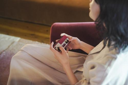 a woman sitting in a chair holding a cell phone at Kominkayado LOOF Sakanoie in Fuefuki