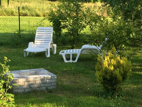 two white chairs and a bench in a yard at Home Apartman in Nagyesztergár