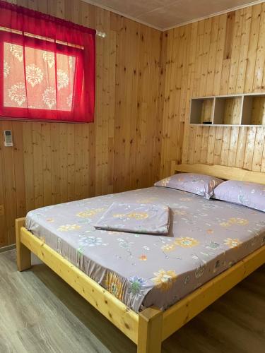 ein Bett in einem Holzzimmer mit einem roten Fenster in der Unterkunft Vila Baciu in Tuzla