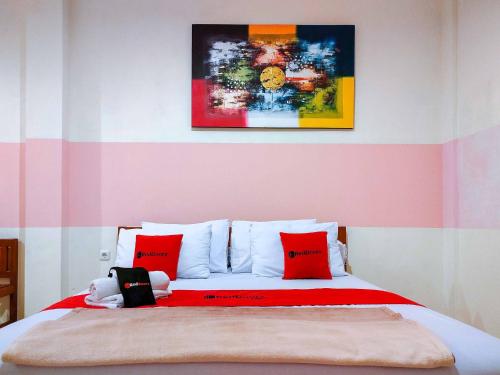 a bedroom with a bed with red pillows and a painting at RedDoorz Near Jalan Jendral Sudirman in Manado
