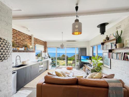 a living room with a brown couch in a kitchen at Riversong & Sea Dreaming in Pambula Beach