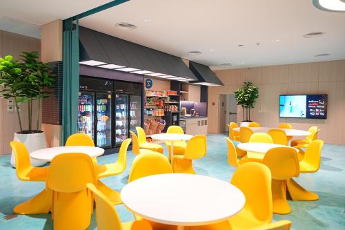 a cafeteria with white tables and yellow chairs at GO Hotel Si Racha at Central Si Racha in Si Racha