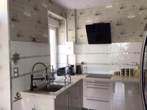 Il comprend une cuisine avec un évier et une télévision murale. dans l'établissement Appartement à 1km des plages avec 2 vélos élec, à Royan