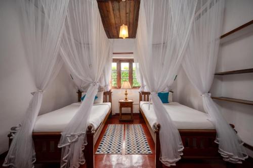 two beds in a room with white curtains at Kelburne Estate in Haputale
