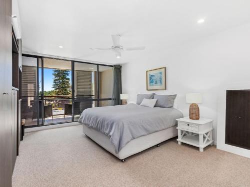 a white bedroom with a bed and a balcony at Beached On Marine Parade in Kingscliff