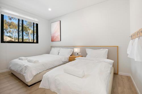 two beds in a white room with a window at Lake View Suites Jindabyne in Jindabyne