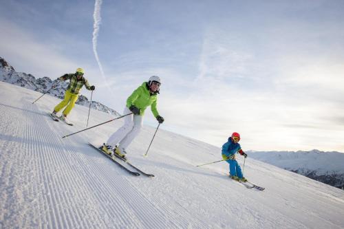 three people are skiing down a snow covered slope at Hotel Tia Apart in Kaunertal