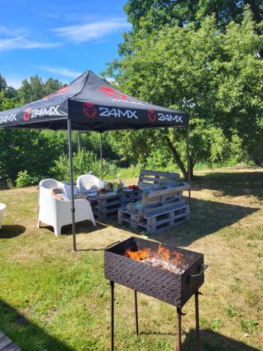 a barbecue under a tent with a table and chairs at Vēverkalni in Vidriži