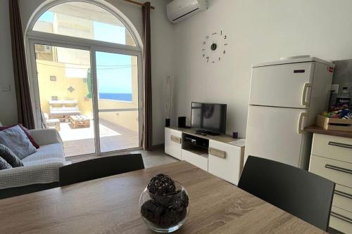 ein Wohnzimmer mit einem Tisch und eine Küche mit einem Kühlschrank in der Unterkunft Serenity Sea-view Maisonette in Marsalforn