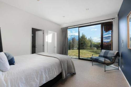 a bedroom with a bed and a chair and a large window at Skye Scape - Jacks Point Retreat in Queenstown