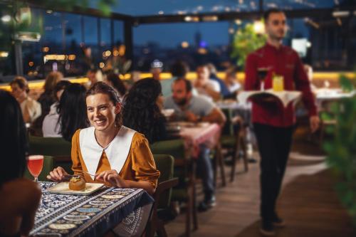 a woman sitting at a table in a restaurant at TbiliSee Hotel in Tbilisi City