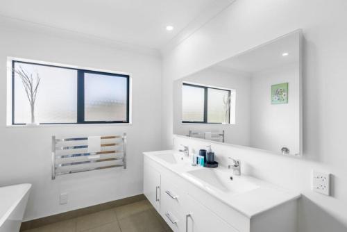 biała łazienka z 2 umywalkami i lustrem w obiekcie Oasis Ode Retreat with pool and spa w Auckland