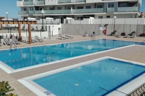 ein großer blauer Pool mit Stühlen und ein Gebäude in der Unterkunft First Class Holiday Tejita WiFiber in Granadilla de Abona