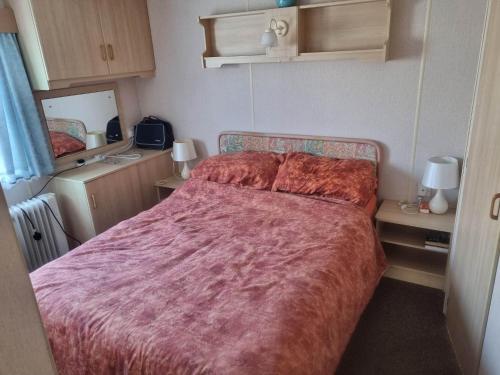 a bedroom with a large bed with a red blanket at Tm8 6 BERTH 2 BEDROOM CARAVAN P in Chapel Saint Leonards