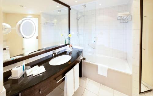 ein Badezimmer mit Waschbecken, Badewanne und Spiegel in der Unterkunft Dorint An der Messe Köln in Köln