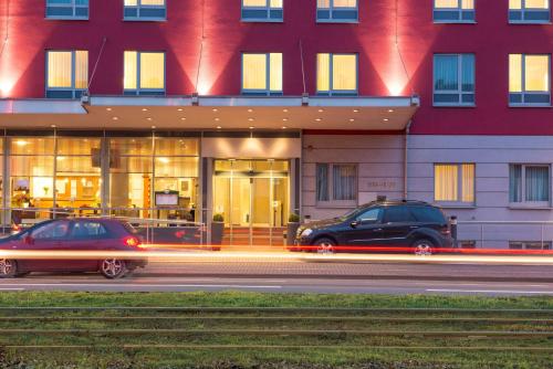 dos coches estacionados frente a un edificio en Essential by Dorint Köln-Junkersdorf en Colonia