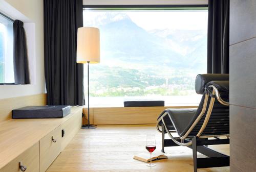 um quarto com uma cadeira e um copo de vinho em Bio & Wellnesshotel Pazeider - Healing Garden above Meran em Marlengo