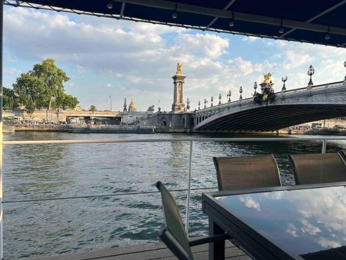 un pont sur une rivière avec une table et des chaises dans l'établissement Péniche de charme au pont Alexandre III, à Paris