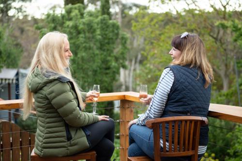 two women sitting on a fence with glasses of wine at Delphi, Adelaide Hills Garden BnB in Mylor