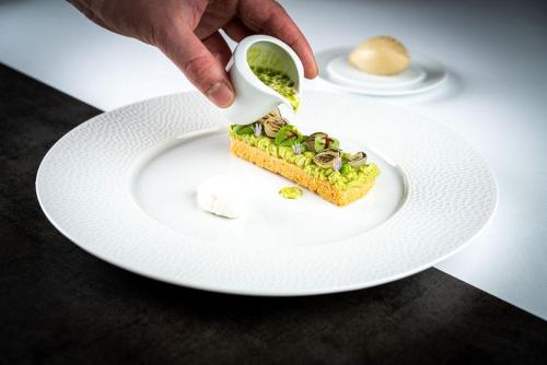 a person pouring a piece of food on a white plate at Hotel Post Andeer in Andeer