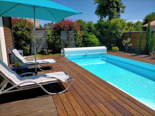 une piscine avec deux chaises et un parasol dans l'établissement Maison familiale avec piscine, à Gujan-Mestras