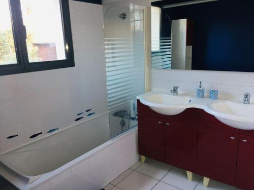 La salle de bains est pourvue de 2 lavabos, d'une baignoire et d'un miroir. dans l'établissement Maison familiale avec piscine, à Gujan-Mestras