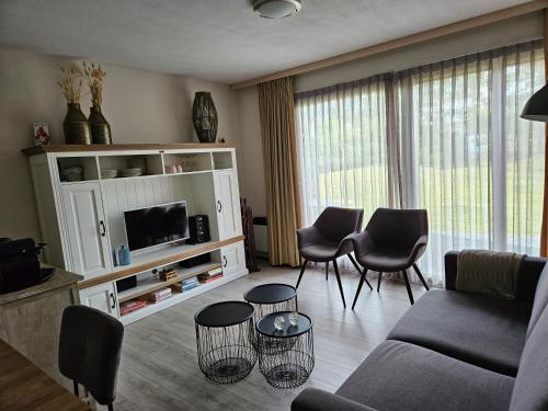 een woonkamer met een bank en stoelen en een tv bij De Kapershut in Hollum