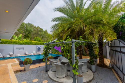 eine Terrasse mit Stühlen, einer Palme und einem Pool in der Unterkunft 3 Bedroom Platinum Pool Villa Smooth as Silk in Ban Khlong Haeng