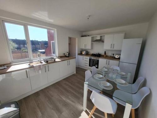 cocina con mesa de cristal y armarios blancos en Coventry Stays - Terraced House en Wyken