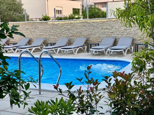 a row of lounge chairs next to a swimming pool at Apartments & rooms Stella Adriatica in Murter