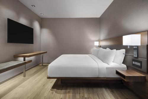 een slaapkamer met een wit bed en een televisie bij AC Hotel by Marriott Lansing University Area in Lansing