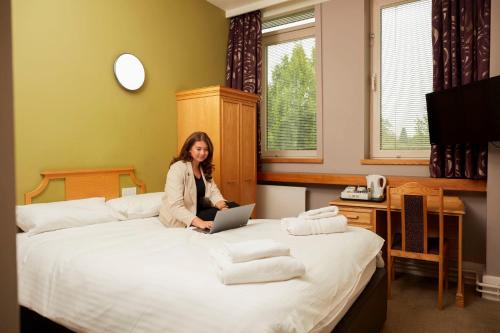 una mujer sentada en una cama con un portátil en Kents Hill Park Training & Conference Centre, en Milton Keynes