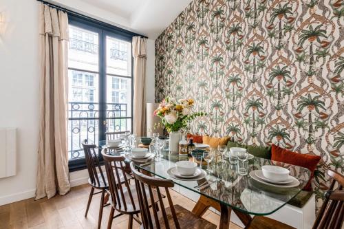 une salle à manger avec une table, des chaises et du papier peint avec des palmiers dans l'établissement Appartement Pastourelle du Marais - Welkeys, à Paris
